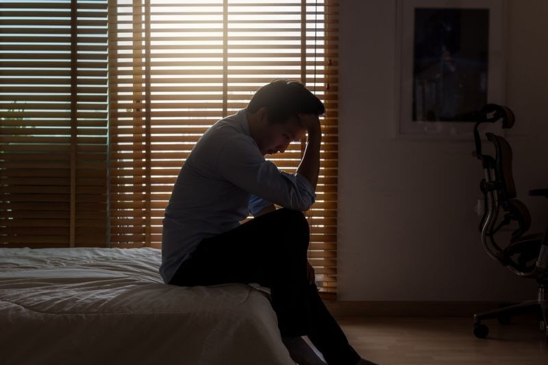 Depression Definition | Mann sitzt traurig im Dunkeln auf dem Bett